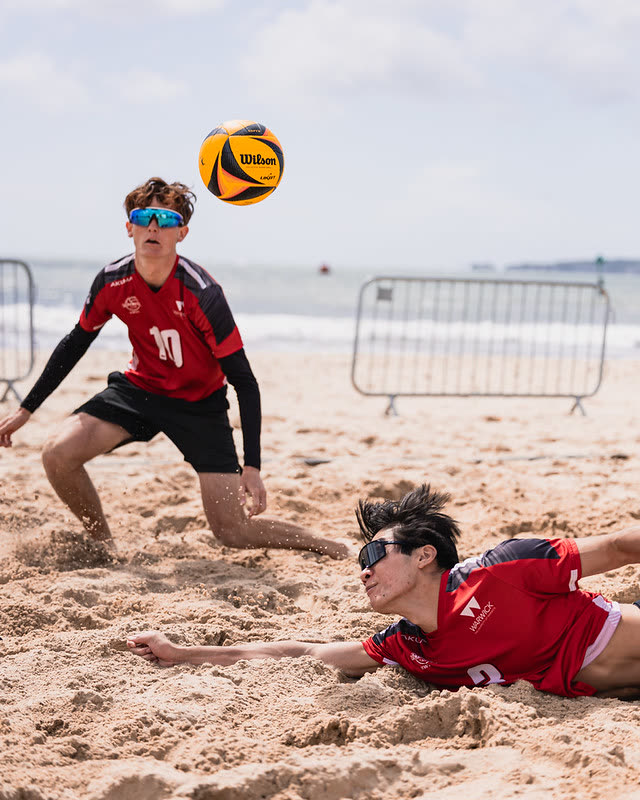 Two university beach volleyball players diving for the ball during a BUCS competition on the sand